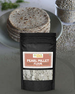 Stone-ground bajra flour pack with stacked rotis and pearl millet grains nearby
