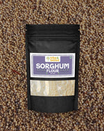 Stone-ground jowar flour in a black ziplock pouch on sorghum grains background